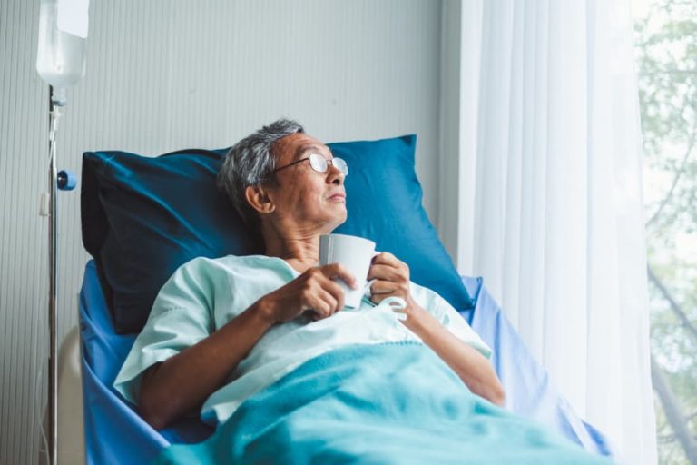 Patient holding mug and looking out window while receiving infusion treatment