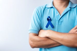 Person with arms folded wearing blue ribbon in support of colon cancer awareness