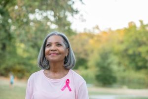 Patient walking in park wearing pink shirt with pink ribbon supporting breast cancer awareness