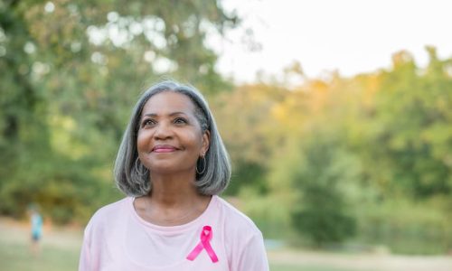Patient walking in park wearing pink shirt with pink ribbon supporting breast cancer awareness