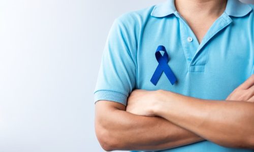 Person with arms folded wearing blue ribbon in support of colon cancer awareness