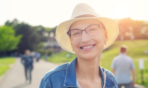 Person with hair loss from chemotherapy smiling outside on a sunny day